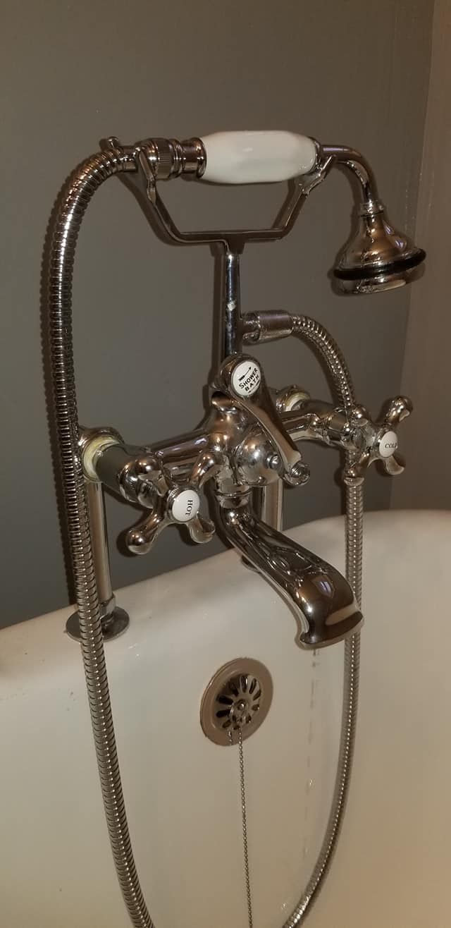 Chrome-colored bathtub faucet with a showerhead and white porcelain handles.