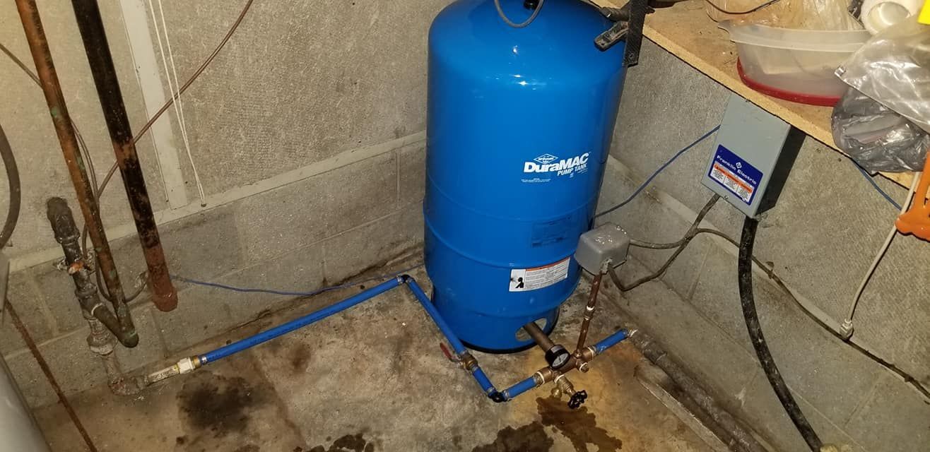 Blue water pressure tank in a basement with concrete walls and floor.