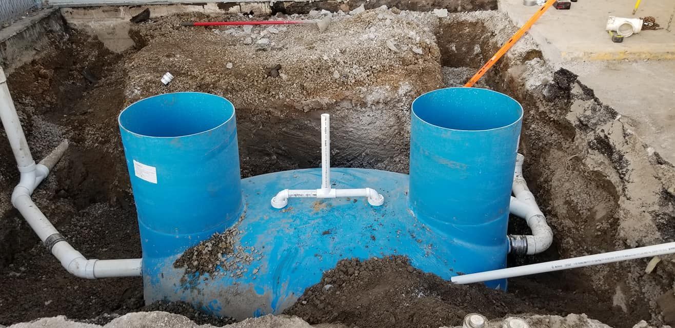 Blue septic tank with white pipes installed in a dirt excavation.