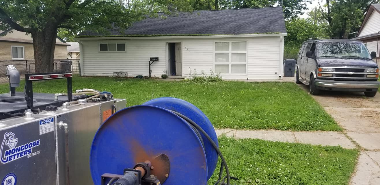 White house with black roof, green lawn, black van parked in driveway, and a blue reel.