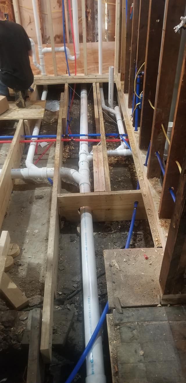Plumbing pipes and framing in a construction setting. A person is visible, working on the plumbing.