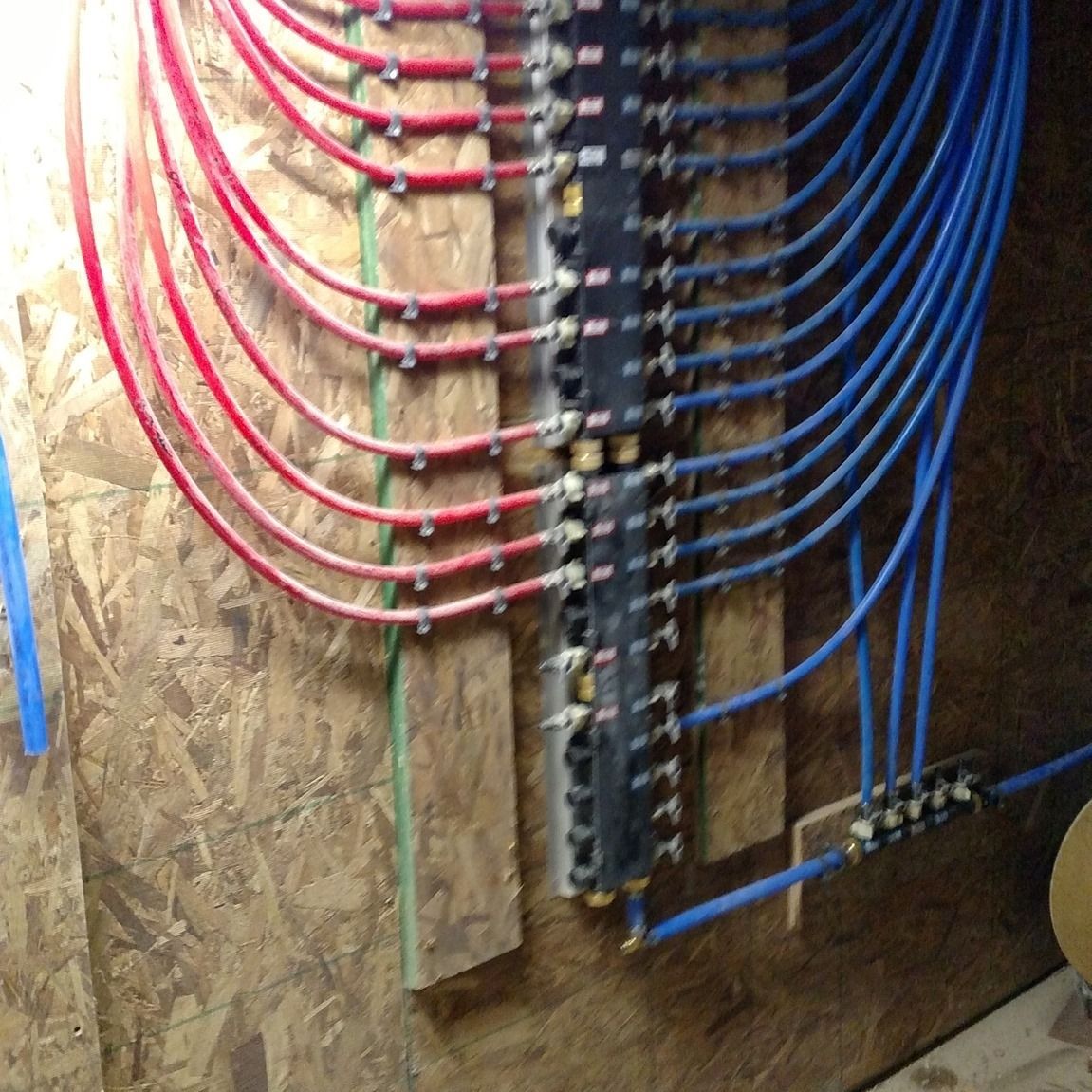 Pipes connected to a plumbing manifold: red and blue PEX tubing on a wooden wall.