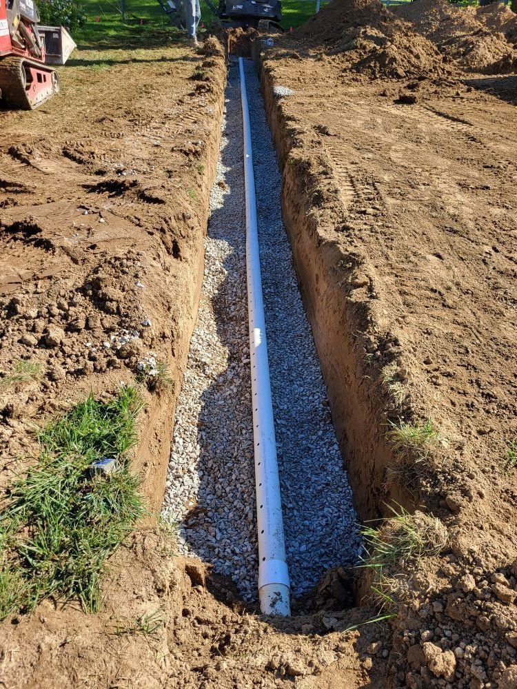 Trench with perforated pipe surrounded by gravel. Construction project outdoors, daylight.