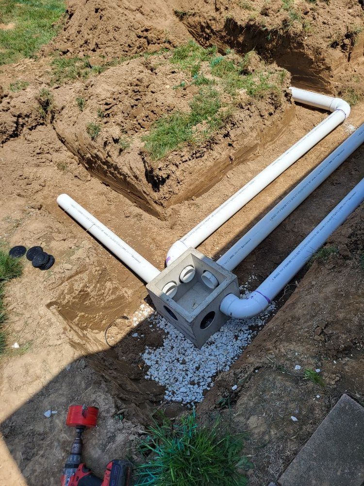PVC pipes connected to a concrete box in a trench; part of an underground drainage system.