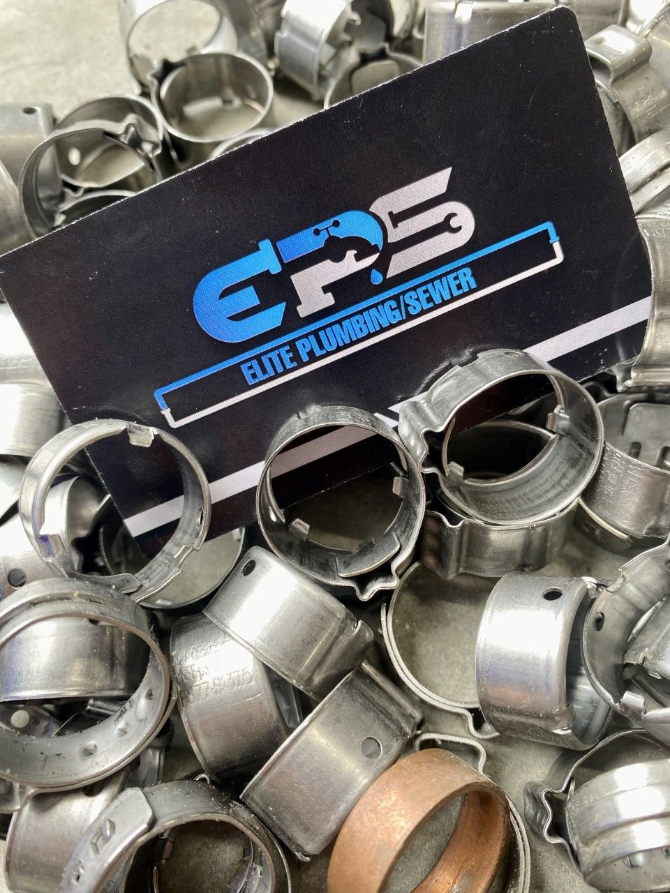 Pile of metal plumbing clamps with a business card from 