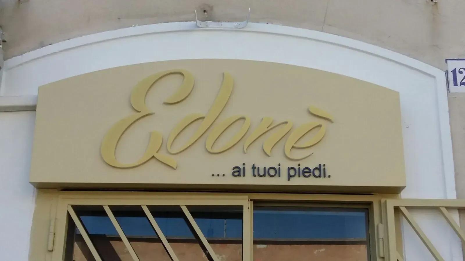 Insegna del negozio con la scritta “Edoa” e lo slogan “... ai tuoi piedi.” su una facciata color crema