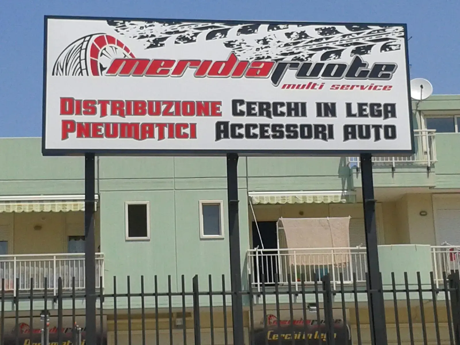 Negozio con grande insegna pubblicitaria per la distribuzione di pneumatici, freni, batterie e accessori per auto.