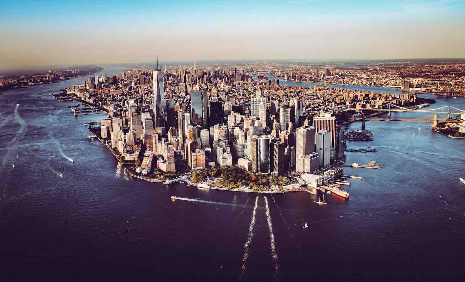 New York City skyline from above, buildings surrounded by water under a clear sky.