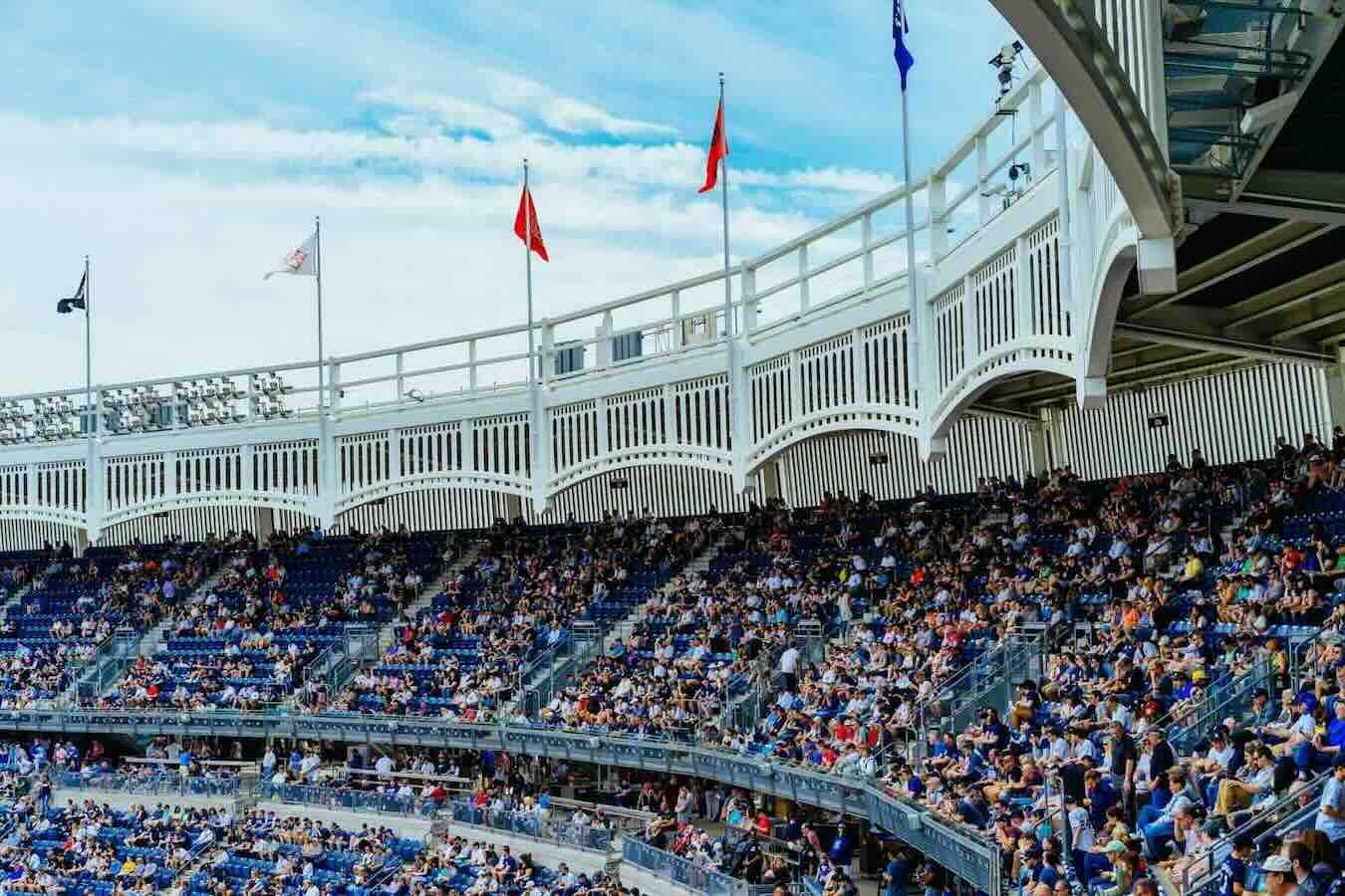 Large crowd at Yankee Stadium during a baseball game, blue seats, white facade, flags waving in the background.