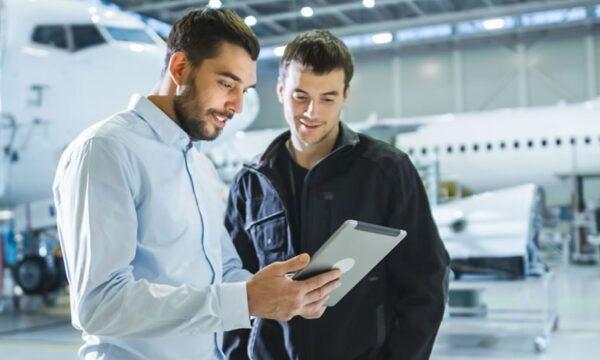 Two men are looking at a tablet in a hangar.