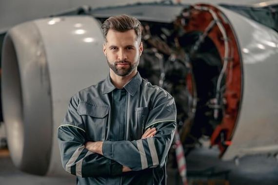 A man is standing in front of an airplane engine with his arms crossed.