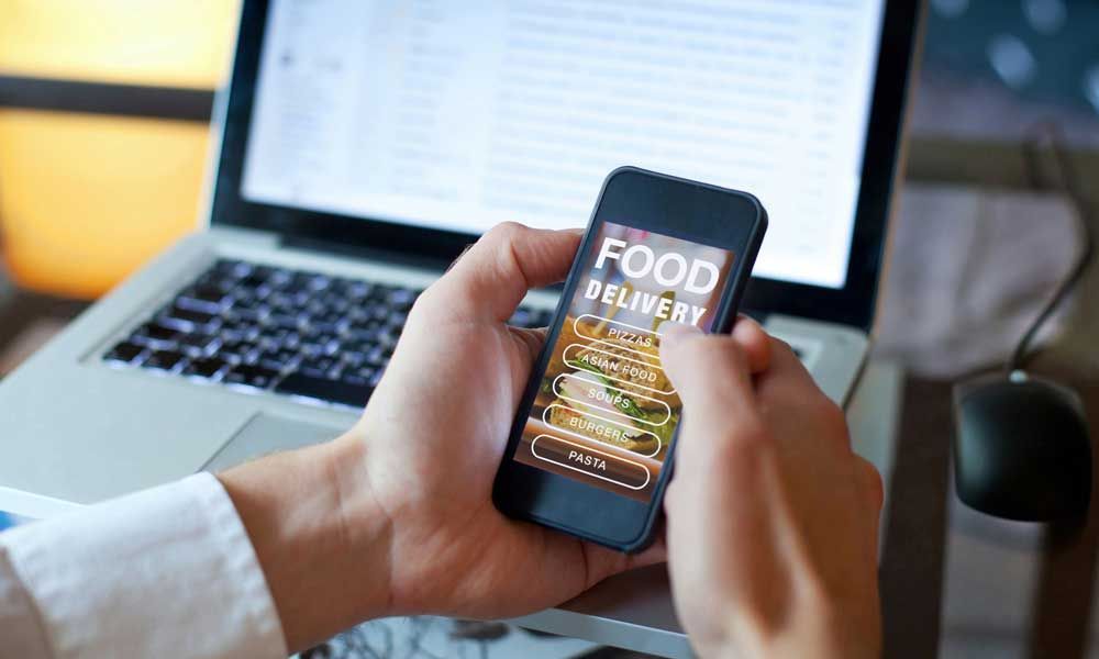 A person is holding a cell phone in front of a laptop.