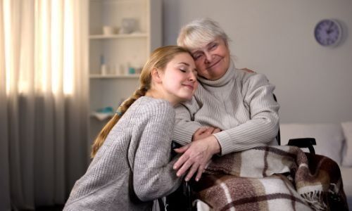 A young girl is hugging an older woman in a wheelchair.