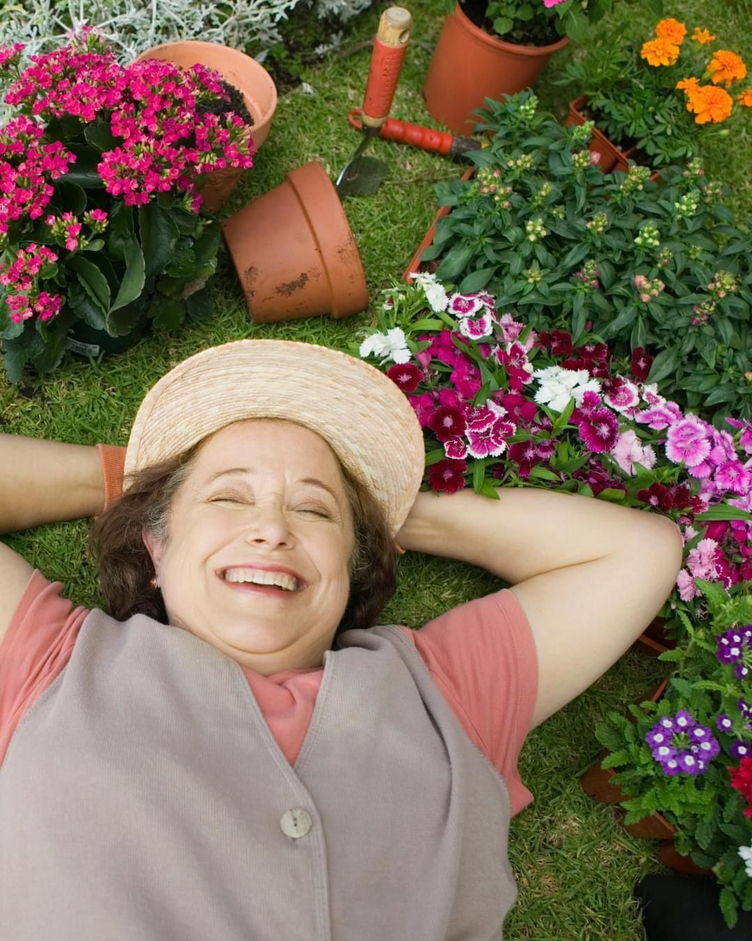 A woman in a straw hat is laying on the grass surrounded by flowers A woman in a straw hat is laying on the grass surrounded by flowers