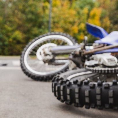 Motorcycle on its side on asphalt, blue and white with black tires, blurred background.