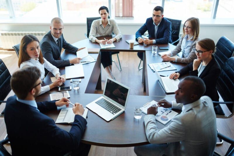 Business team in a meeting at a large table; diverse group reviewing documents.
