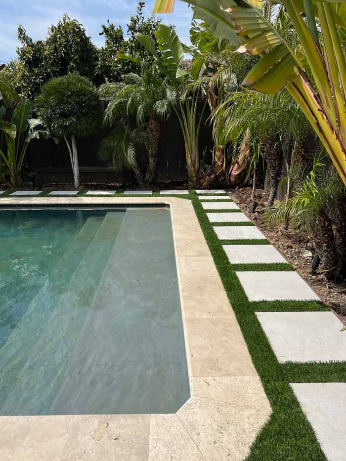 A swimming pool with a walkway surrounded by trees and grass.