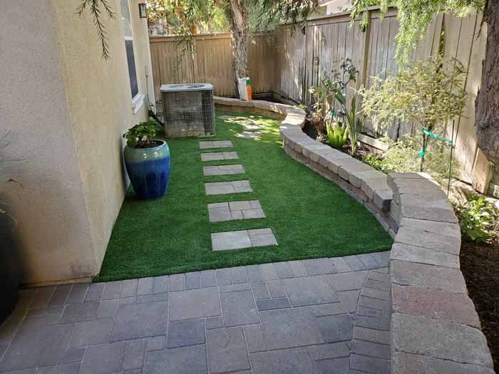 A backyard with a brick walkway and a potted plant.