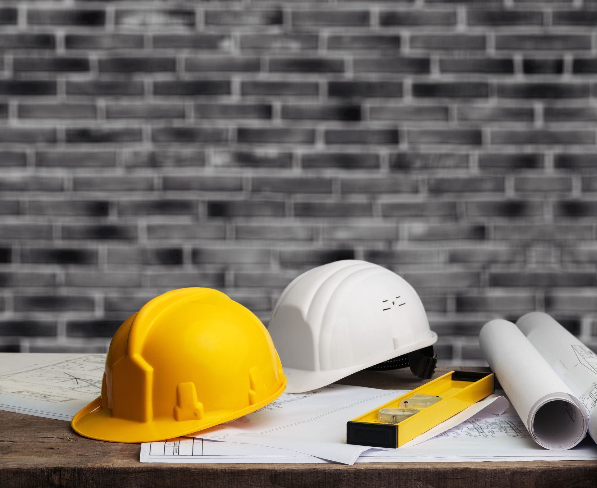 two hard hats , a level , and blueprints are on a wooden table .