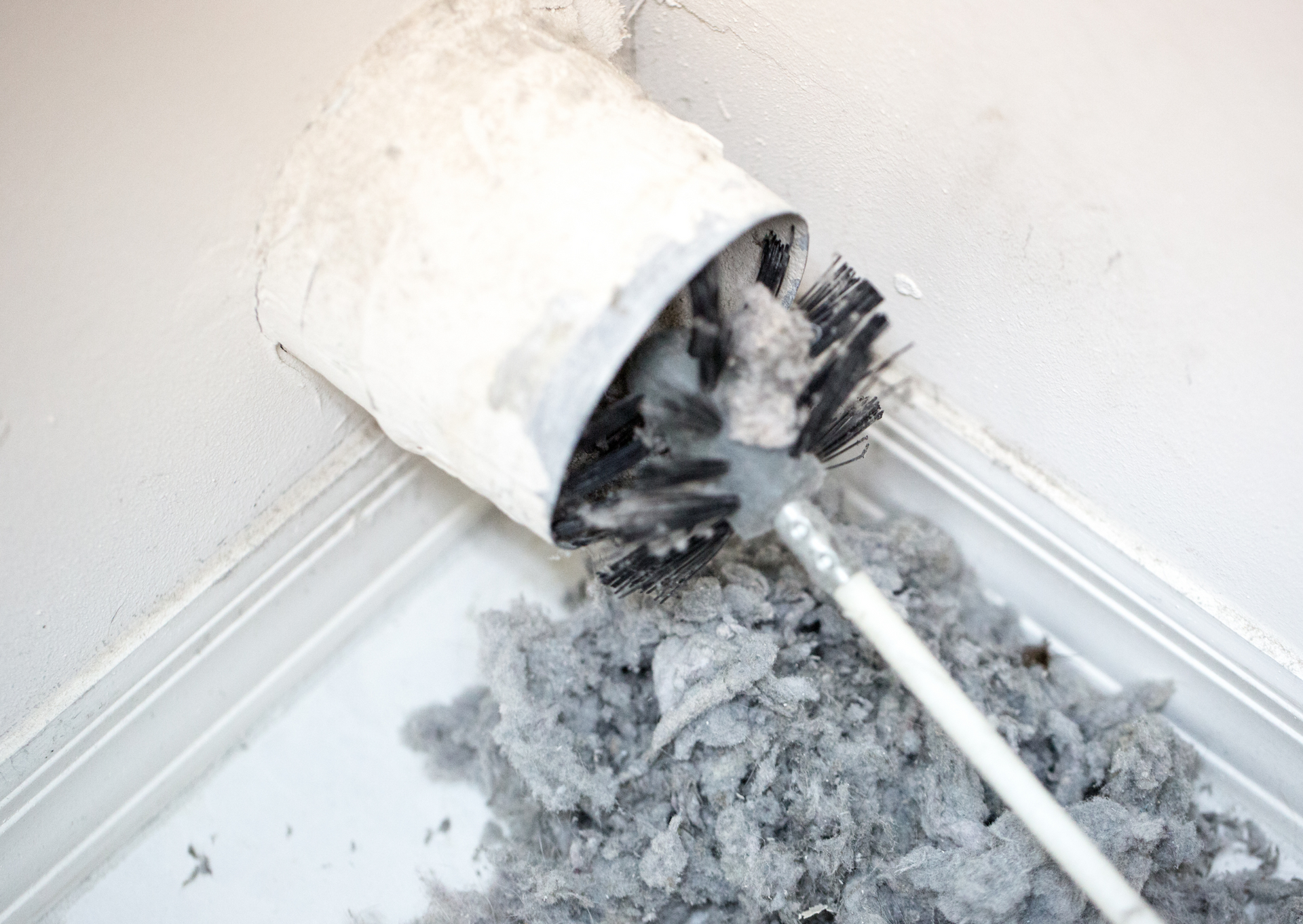 Cleaning a dryer vent with a brush, removing a large pile of lint.