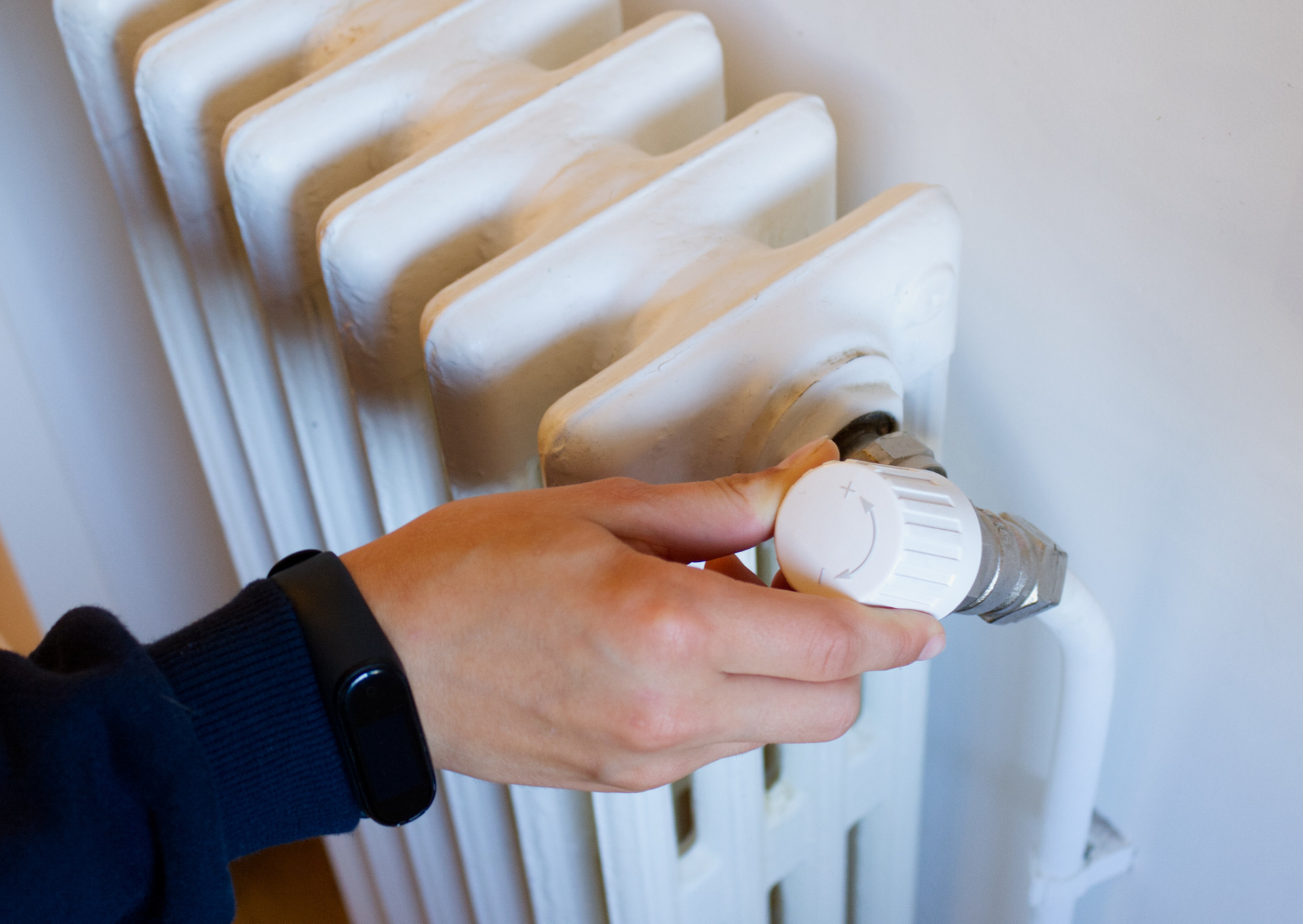 Hand turning the dial on a white radiator.