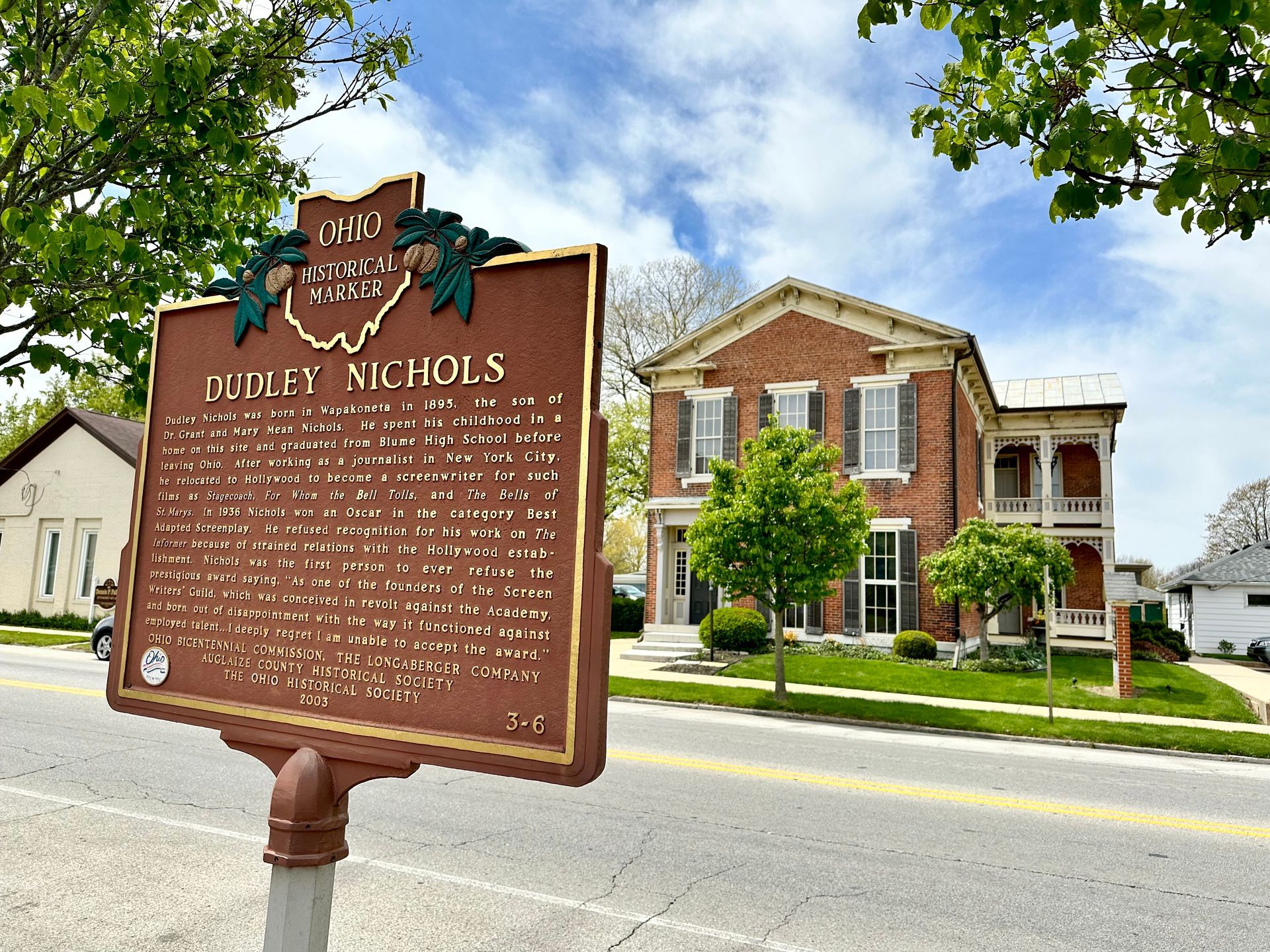 A historical marker for Dudley Nichols is in front of a brick building.