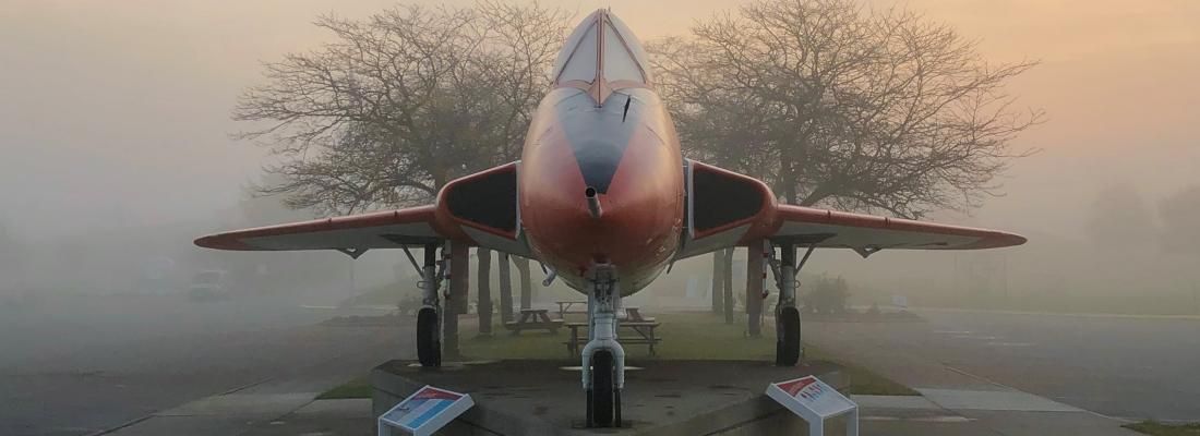 A fighter jet is parked in the fog in front of the Armstrong Air & Space Museum.