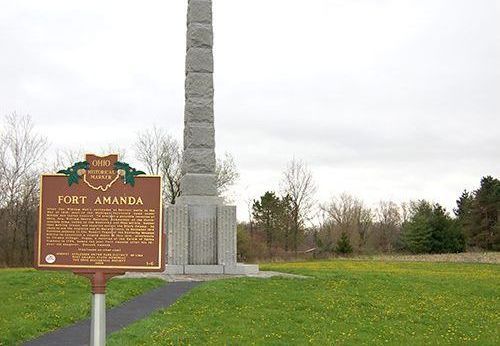 A historical marker for Fort Amanda is sitting in front of a monument.