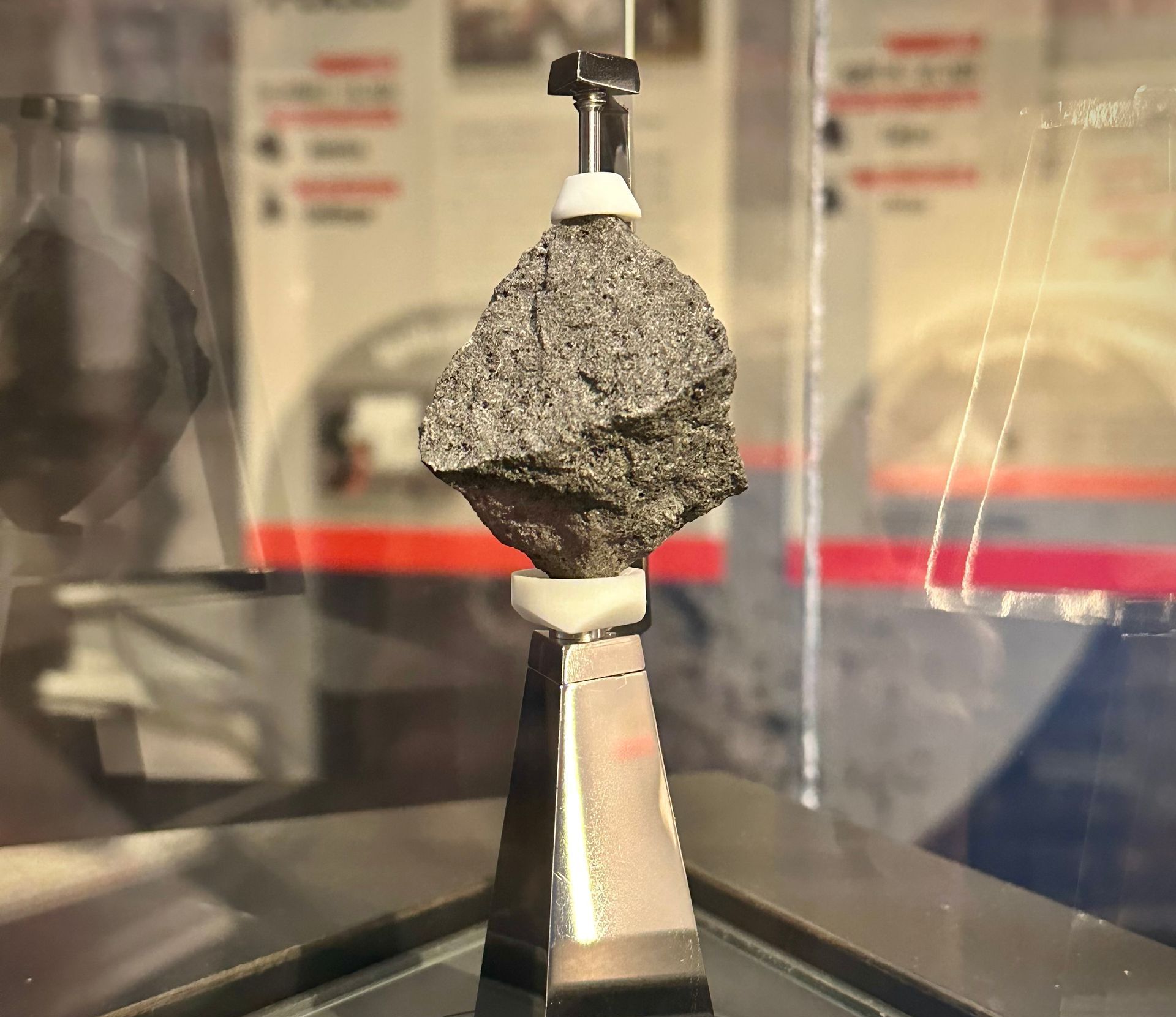 A small moon rock is sitting on top of a metal object in a museum display.