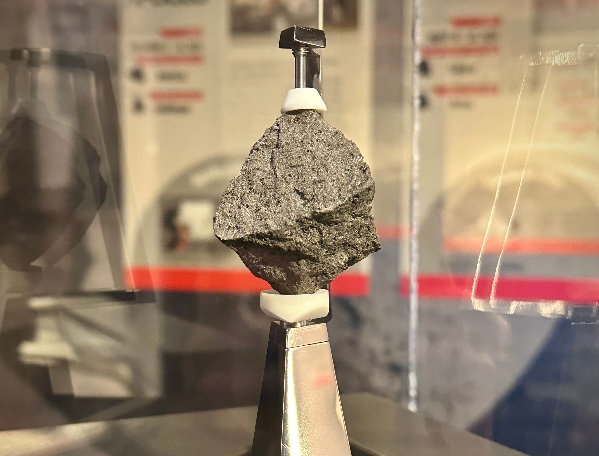 A small moon rock is sitting on top of a metal object in a museum display.