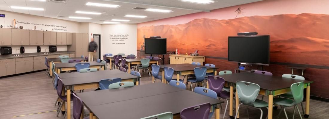 A classroom with tables and chairs and a large picture on the wall.