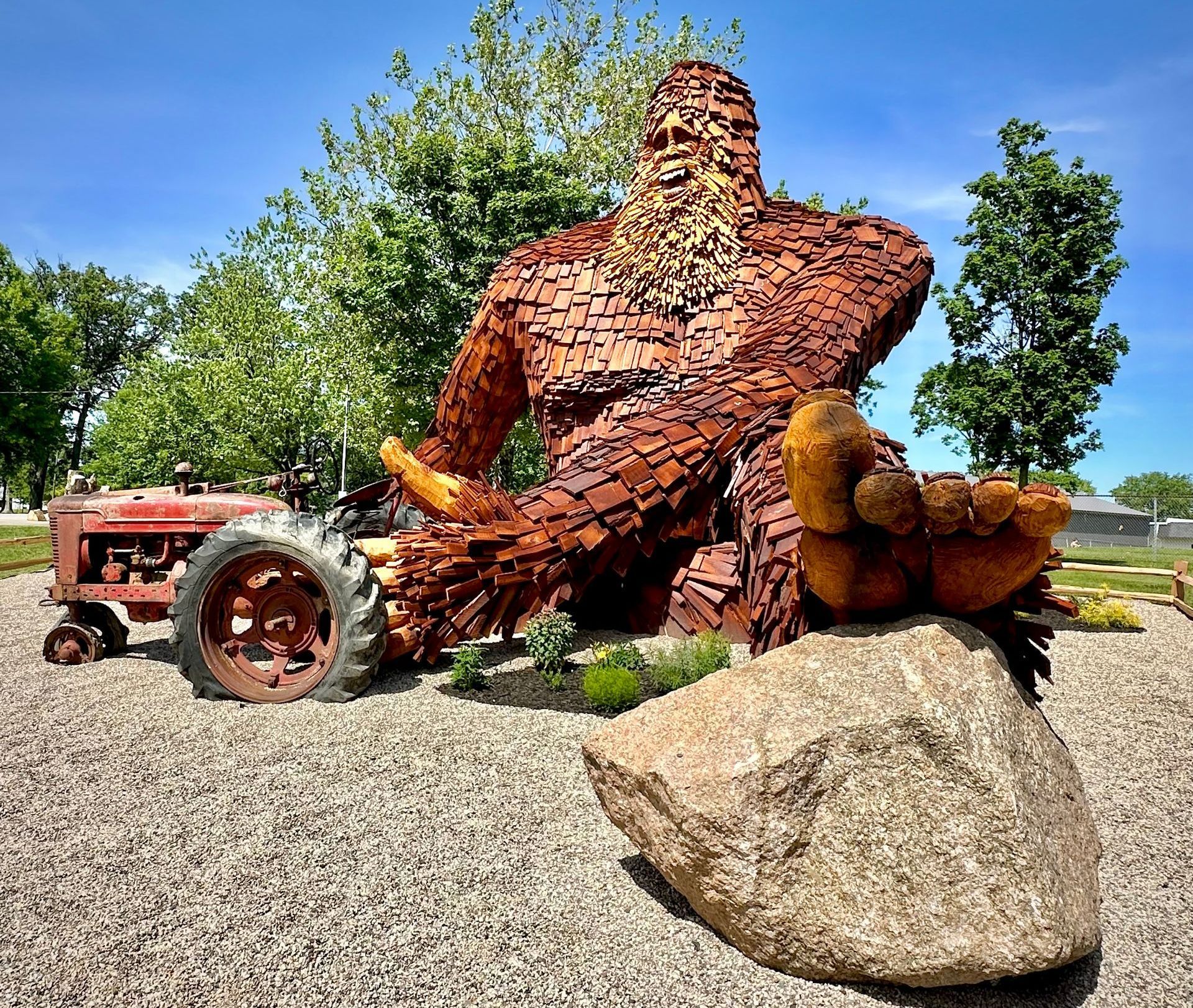 A giant wooden sasquatch statue with tractor in front.