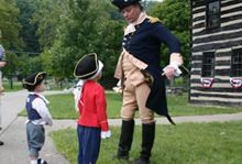 A man in a military uniform is standing next to two children in Carillon Historical Park.