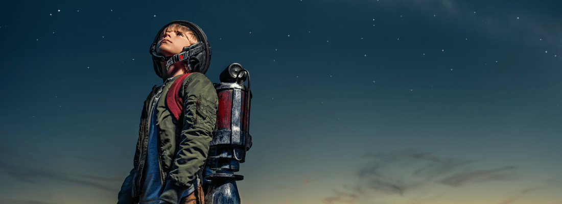 A young boy is wearing a helmet and holding a rocket on his back.