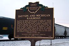 A historical marker for Dayton and Michigan Railroad is in front of a train.