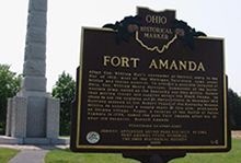A historical marker for Fort Amanda is sitting in front of a monument.