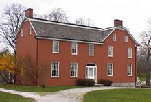 A large red brick house with a white door -- the Johnson Farm and Indian Agence -- is framed in a grassy yard.