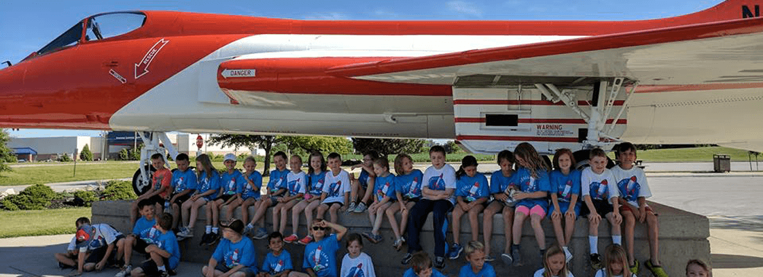 A group of children are posing for a picture in front of a red and white fighter jet.