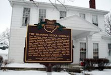 A historical marker for the Shannon Stock Company is in front of a white house covered in snow.
