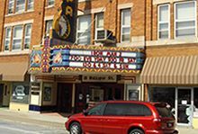 A red minivan is parked in front of a the historic Wapa Theatre.