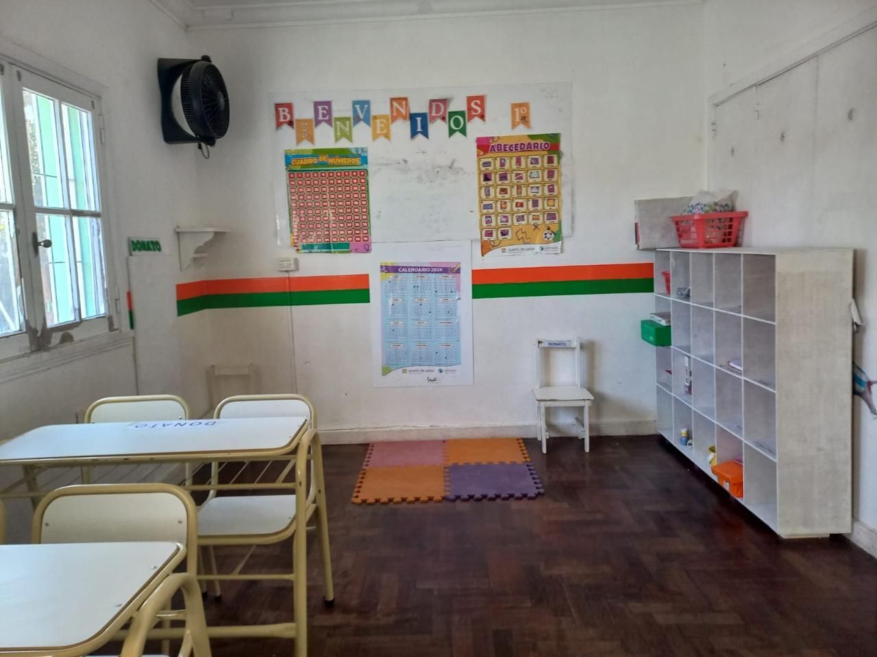 Un aula con mesas y sillas y un estante.