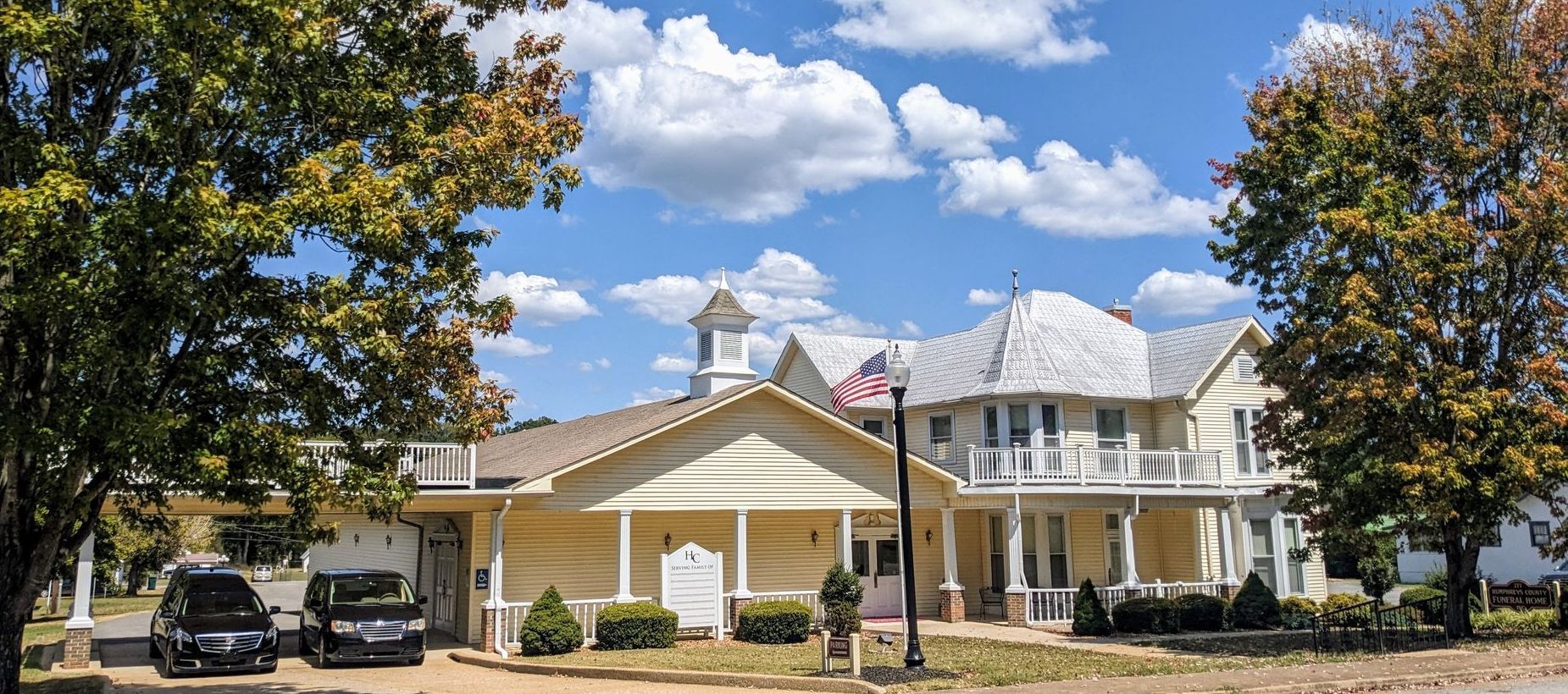 A large house with cars parked in front of it and trees in front of it.