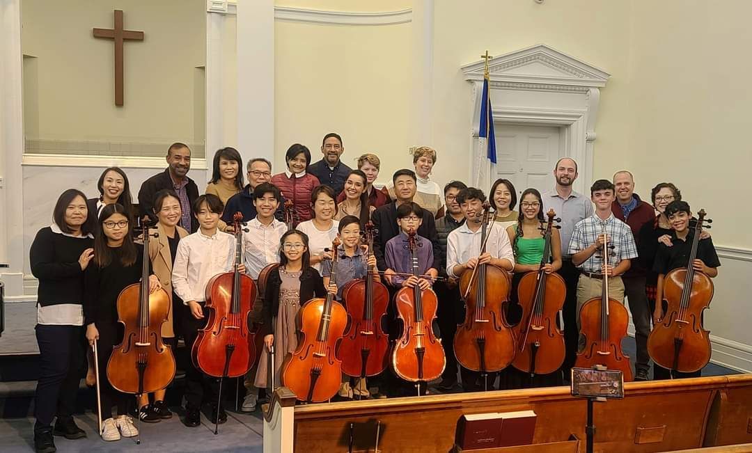 A large group of Koart Academy students standing next to each other holding cello in First Baptist Church.