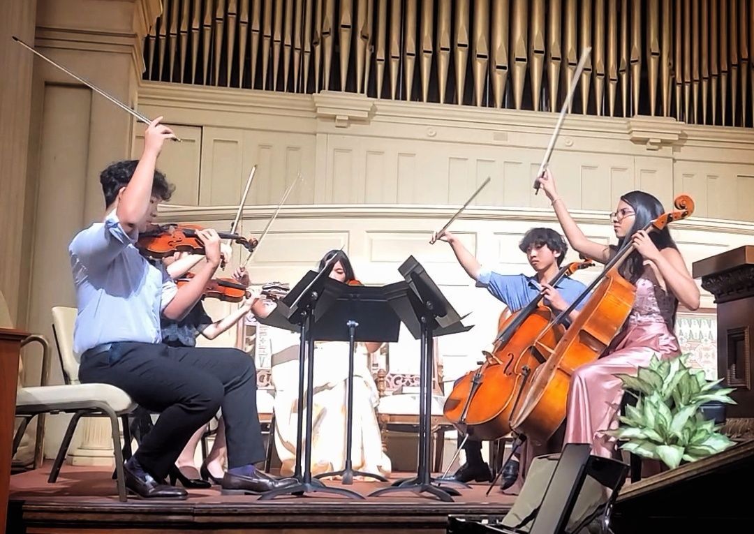 A group of Koart Academy students are playing violins and cello on a stage.