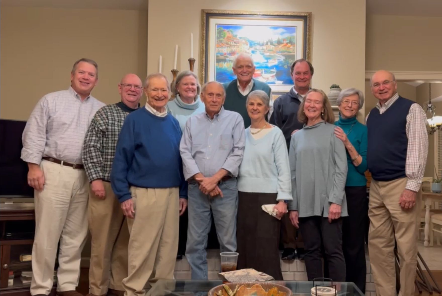 A group of older adults gathered in front of a fireplace in a brightly-lit room.