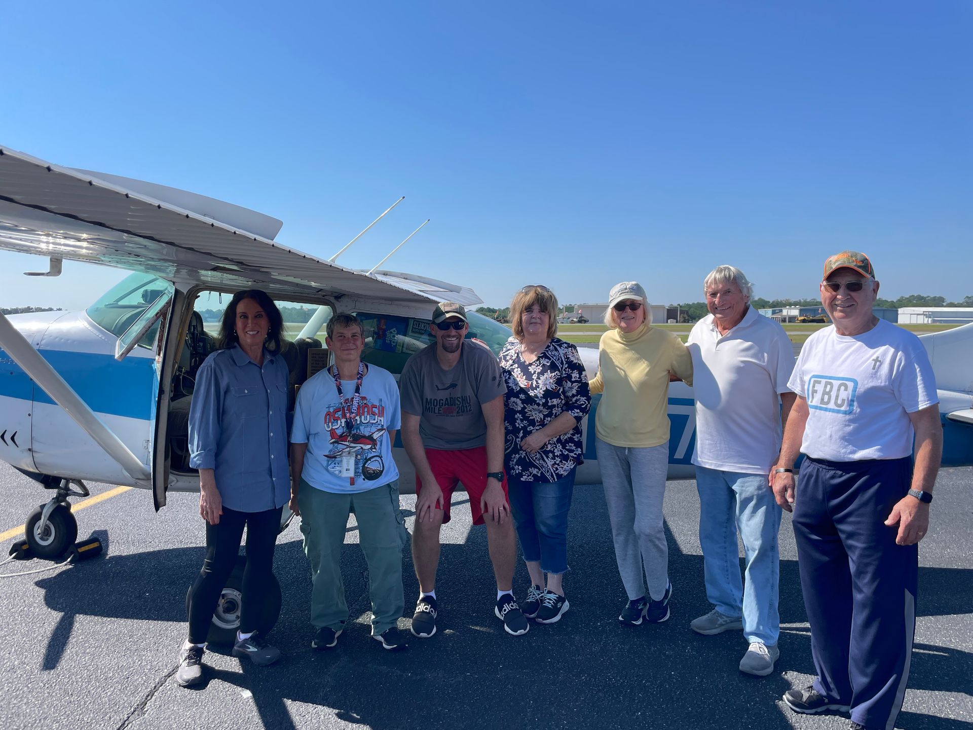 A group of 7 people are standing in front of a small plane.