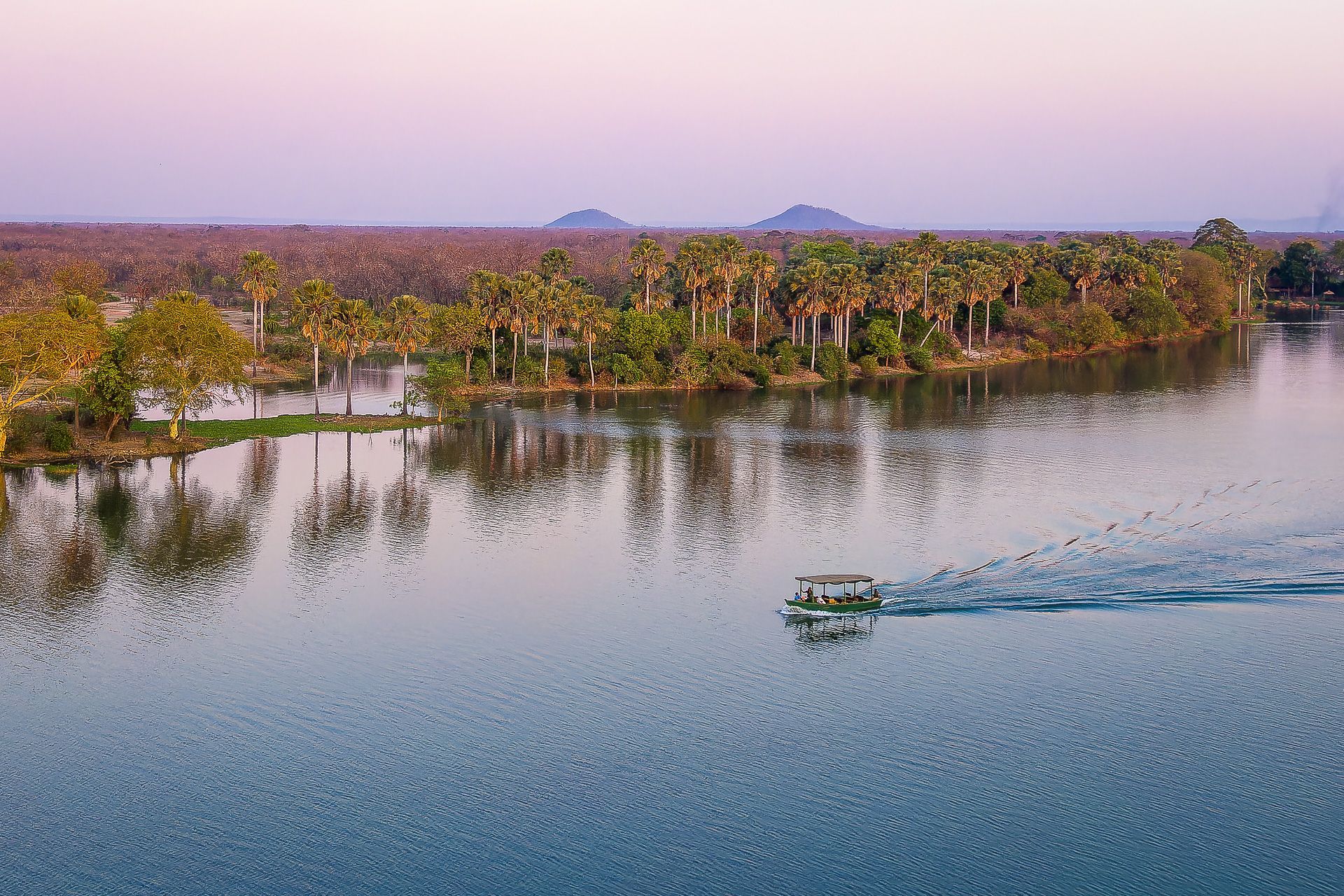 Boat on lake reflects trees at sunset.