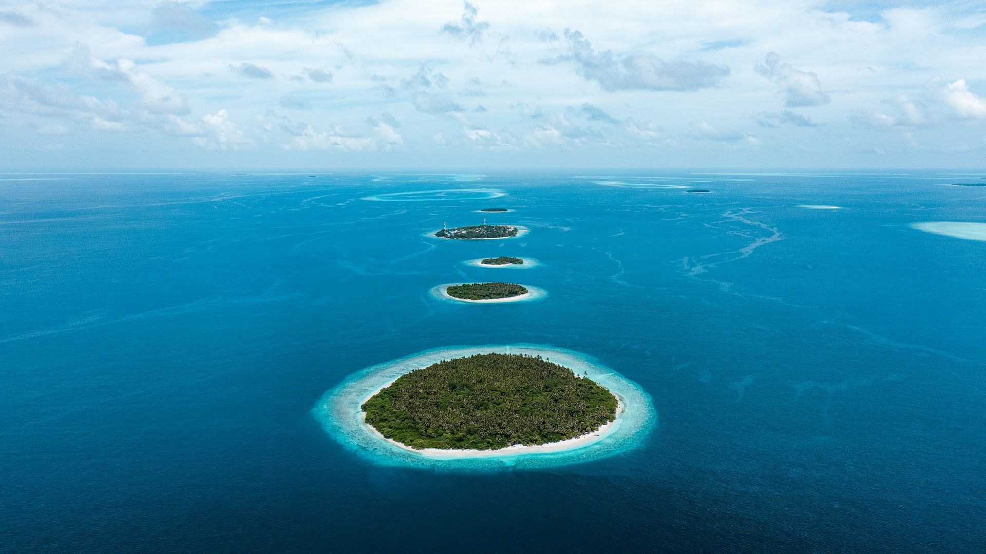 Several small, green islands in a turquoise ocean under a partly cloudy sky.