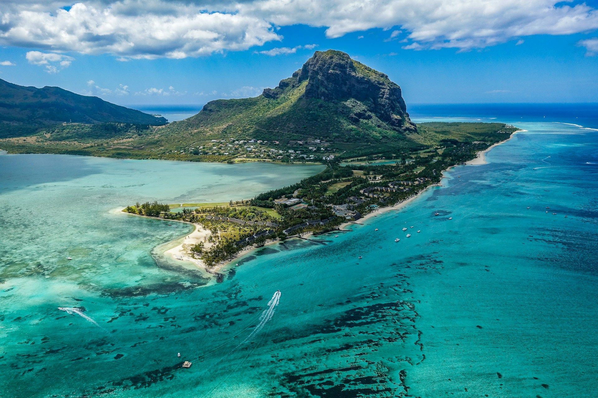 Emerald blue ocean and coastline with mountain in the background under a blue sky.