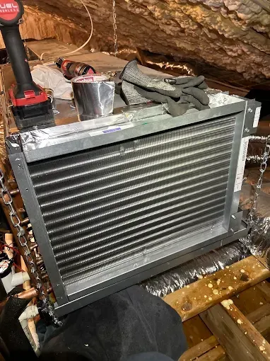 Air conditioner evaporator coil in an attic, with tools and gloves nearby.